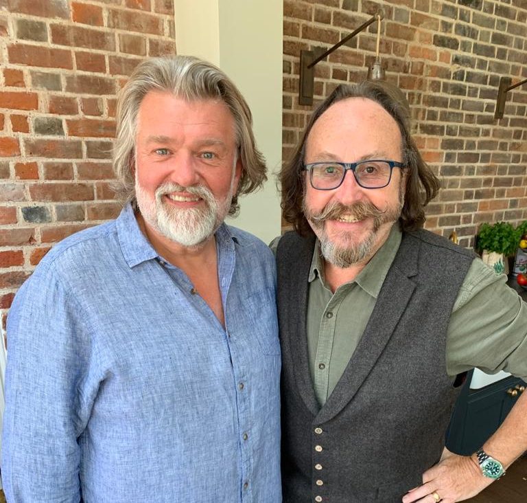 Photograph of Si Kinf and Dave Myers - aka the Hairy Bikers standing next to a red brick wall.